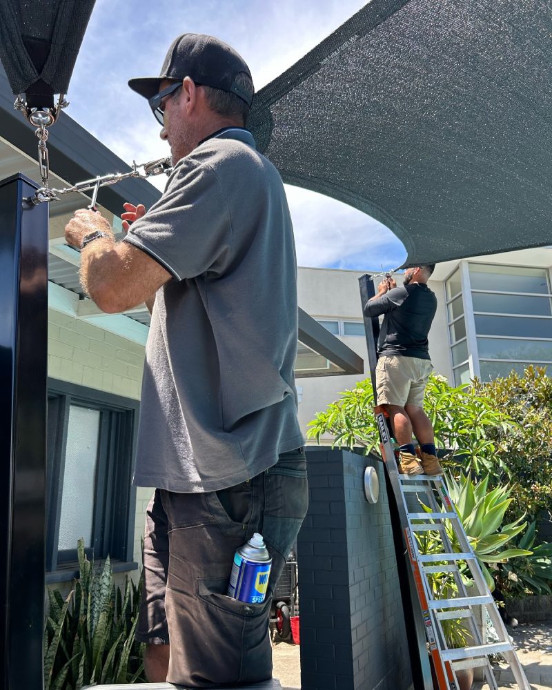 Two Sail City installers tensioning a charcoal shade sail at a Perth home